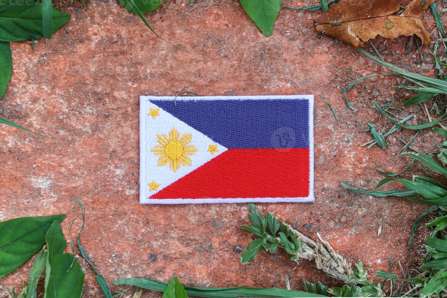 Top view of eco friendly Philippines flag, hand stitched from natural fabric, placed on aged stone with leaves around. Celebrating national pride and sustainability in Southeast Asia. photo