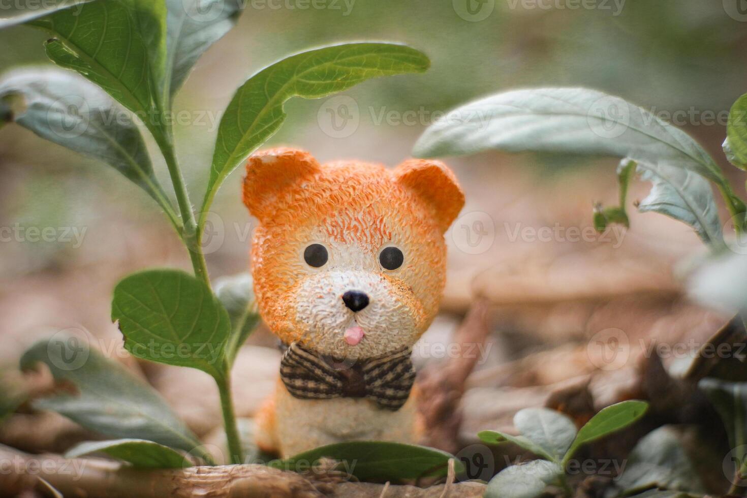 A tiny orange clay dog figurine with big eyes and tongue out, happily sitting under a small tree among green grass. Soft-focus background, playful natural concept representing love for nature. photo