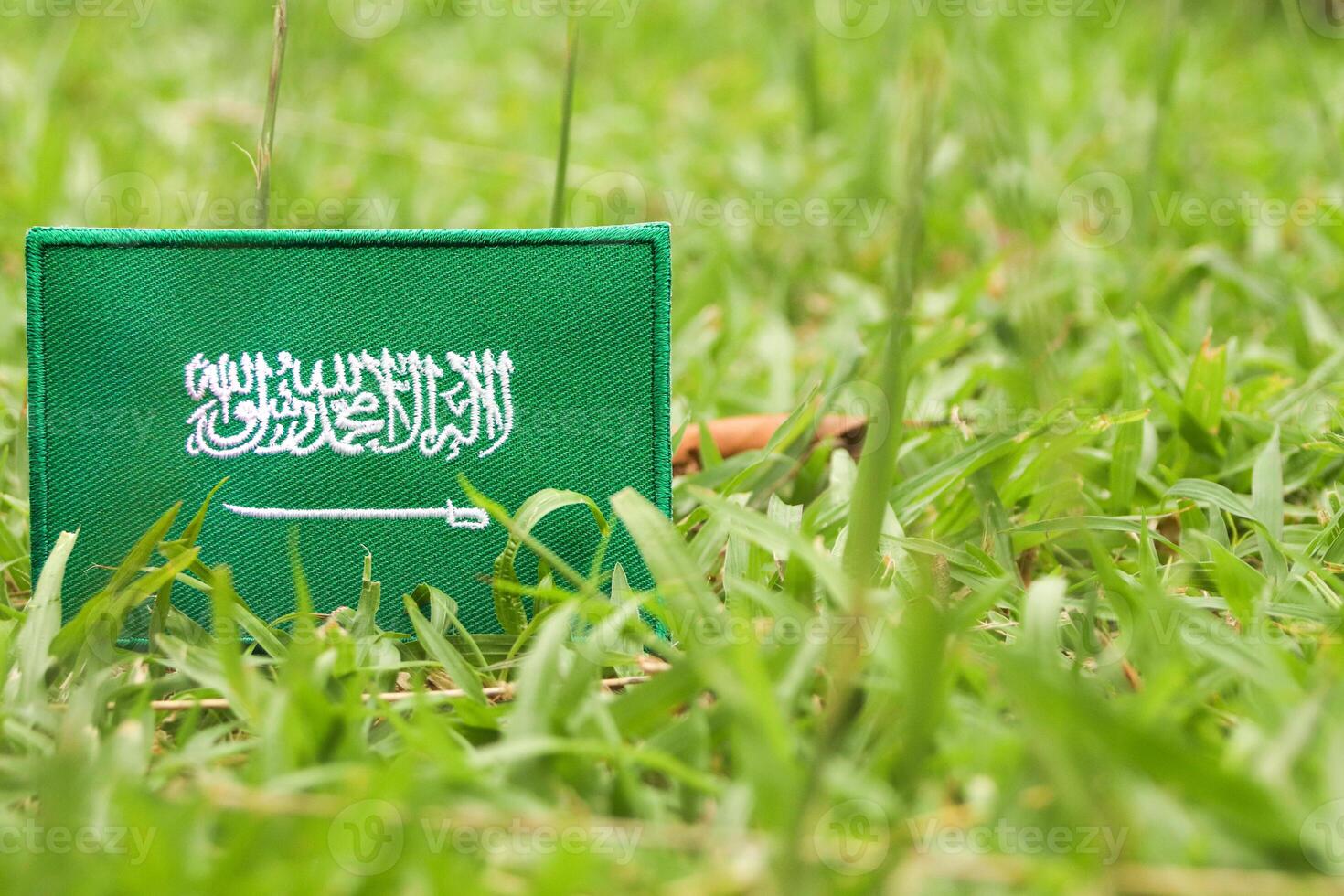 Green-themed Saudi flag made from embroidered fabric, placed on natural grass with open space for text. Ideal for eco concepts and the Middle East Green Initiative. photo