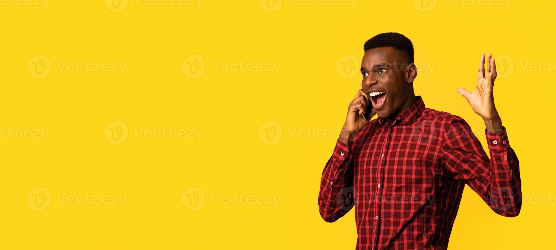 Mobile Communication. Excited African American Guy Emotionally Talking On Cellphone, Having Pleasant Phone Conversation, Standing Isolated Over Yellow Background, Panorama With Copy Space photo