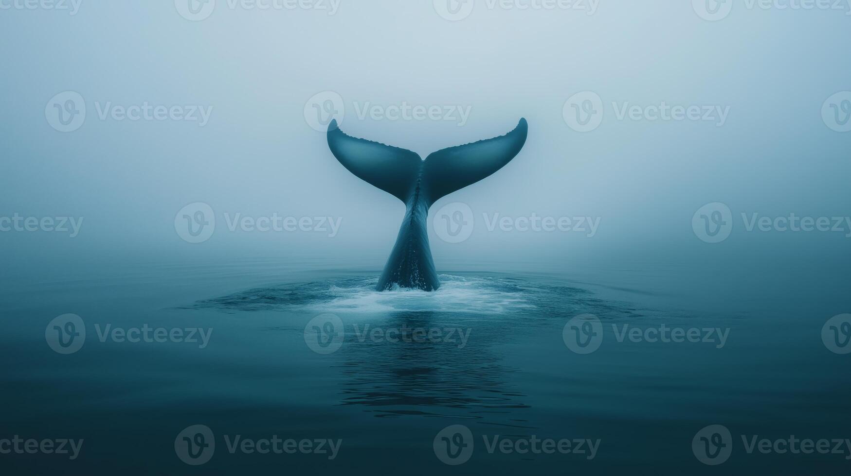 A whale's tail rises above the water, surrounded by mist in a serene ocean setting at dawn. photo