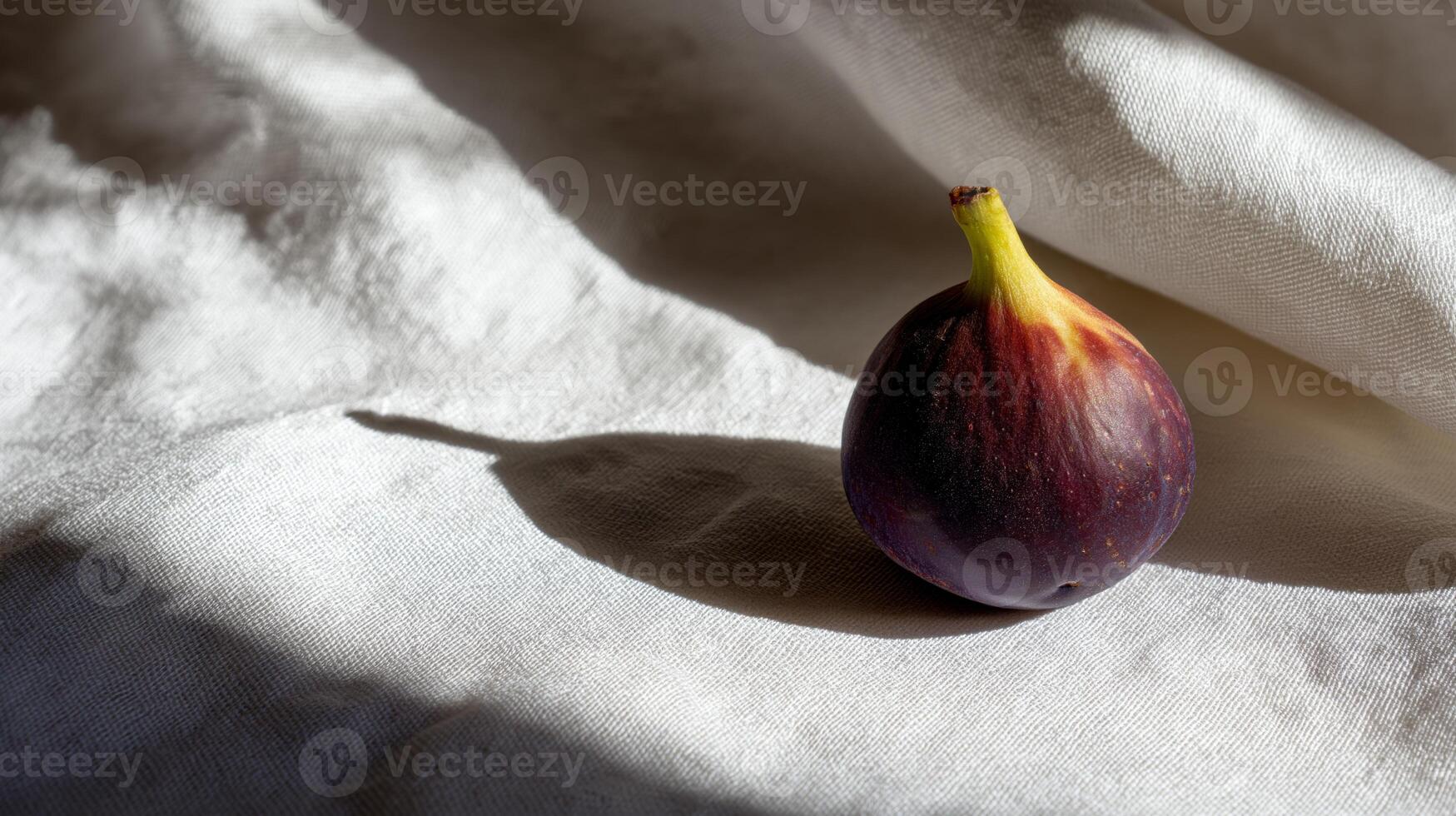 A vibrant fig sits alone on smooth white fabric, illuminated by gentle sunlight in a serene setting. photo