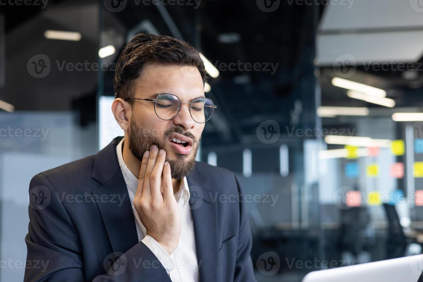 Man suffering from toothache at workplace inside office. Businessman working at workplace sick has gum inflammation. photo
