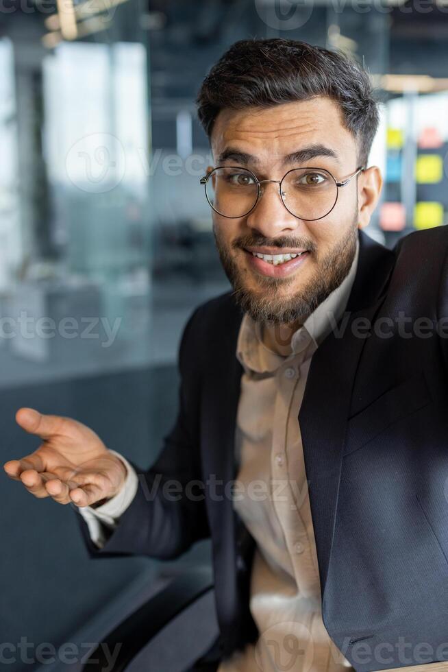 Successful businessman uses phone for call, man in business suit works inside office, looks at camera, remote business meeting, records message. photo