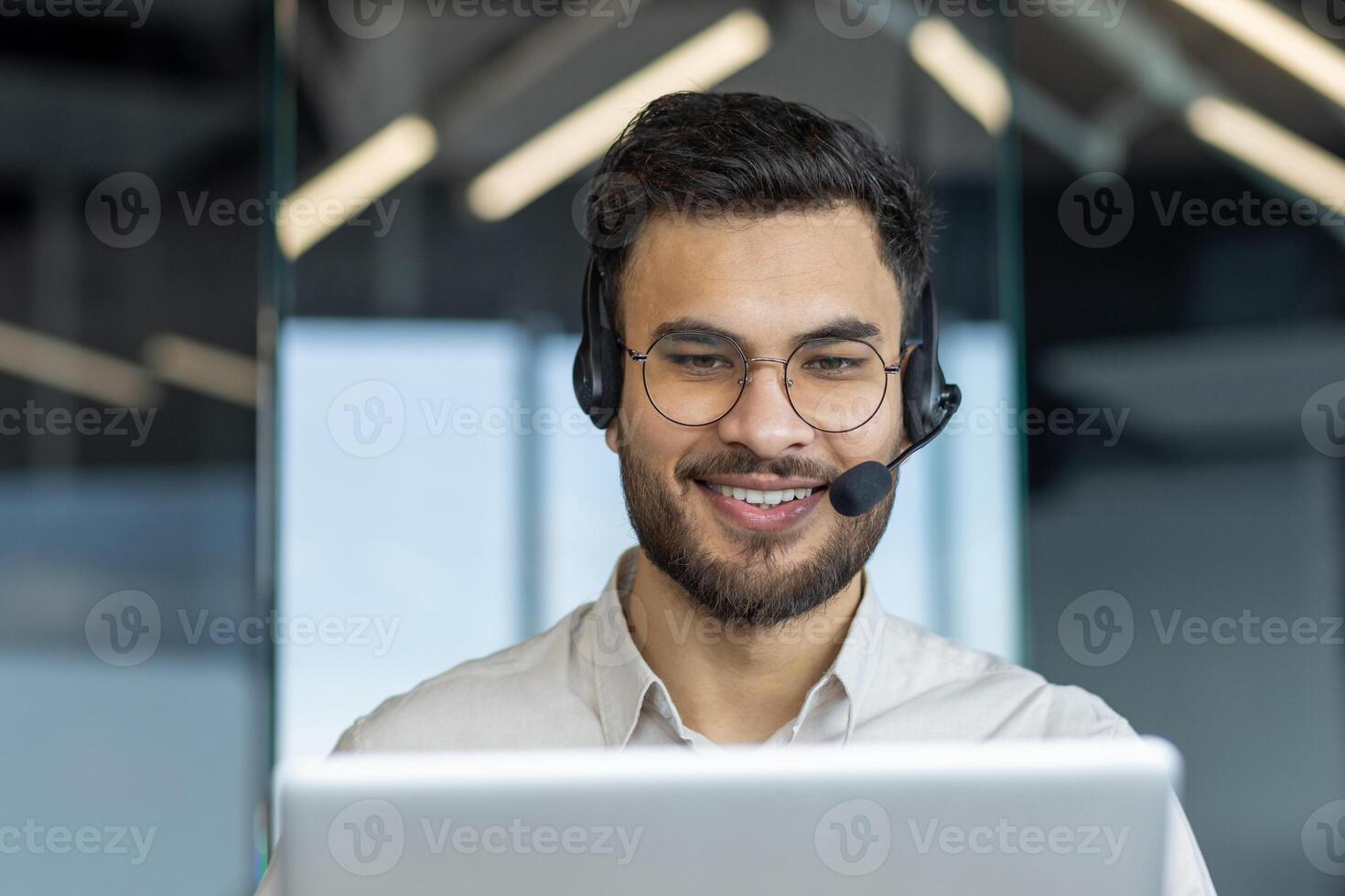 Man with headset close-up smiling, talking and consulting clients remotely. Support service worker at workplace inside office. Consultant at work. photo