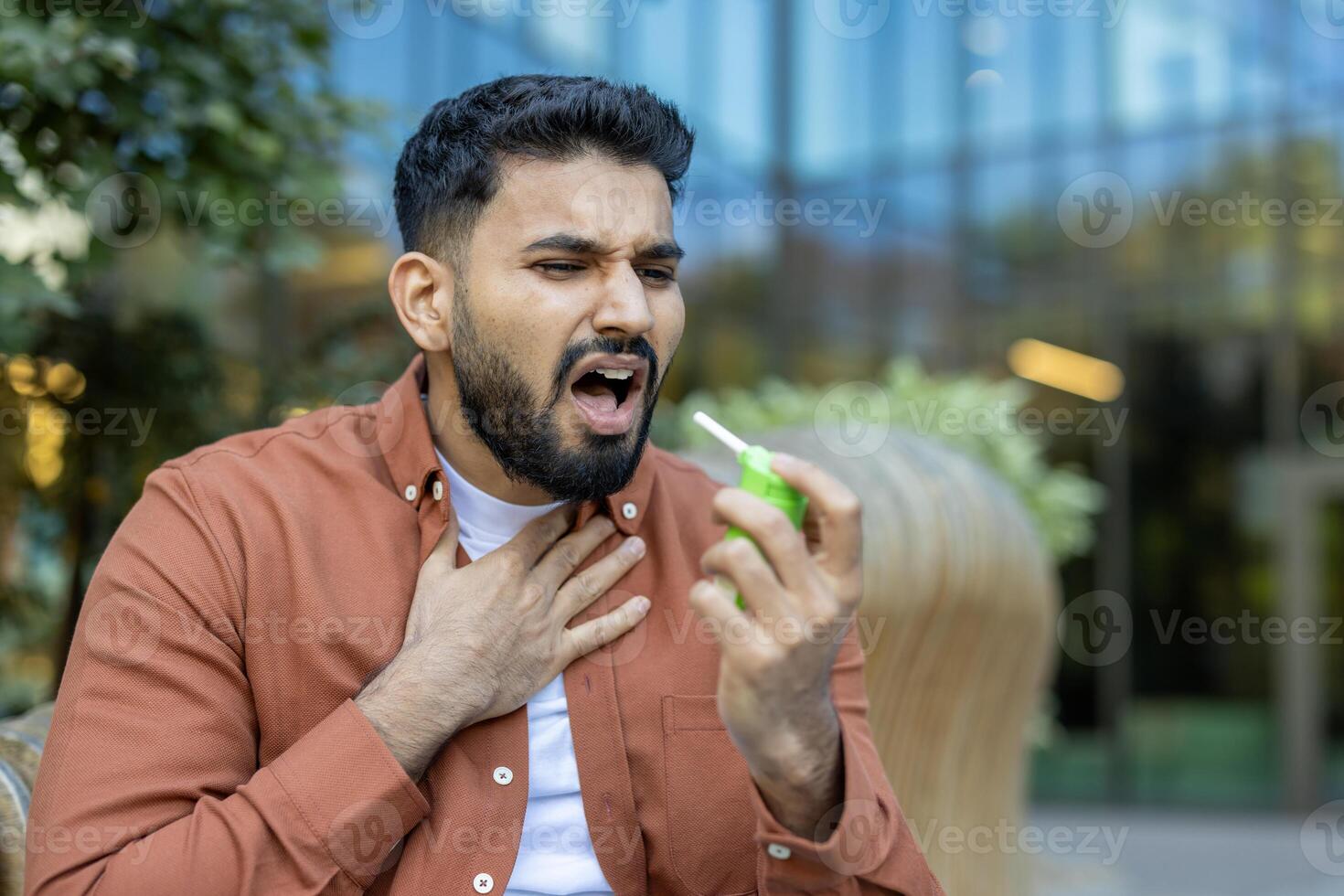A man uses throat spray to soothe his throat and possibly treat angina, with a look of discomfort photo