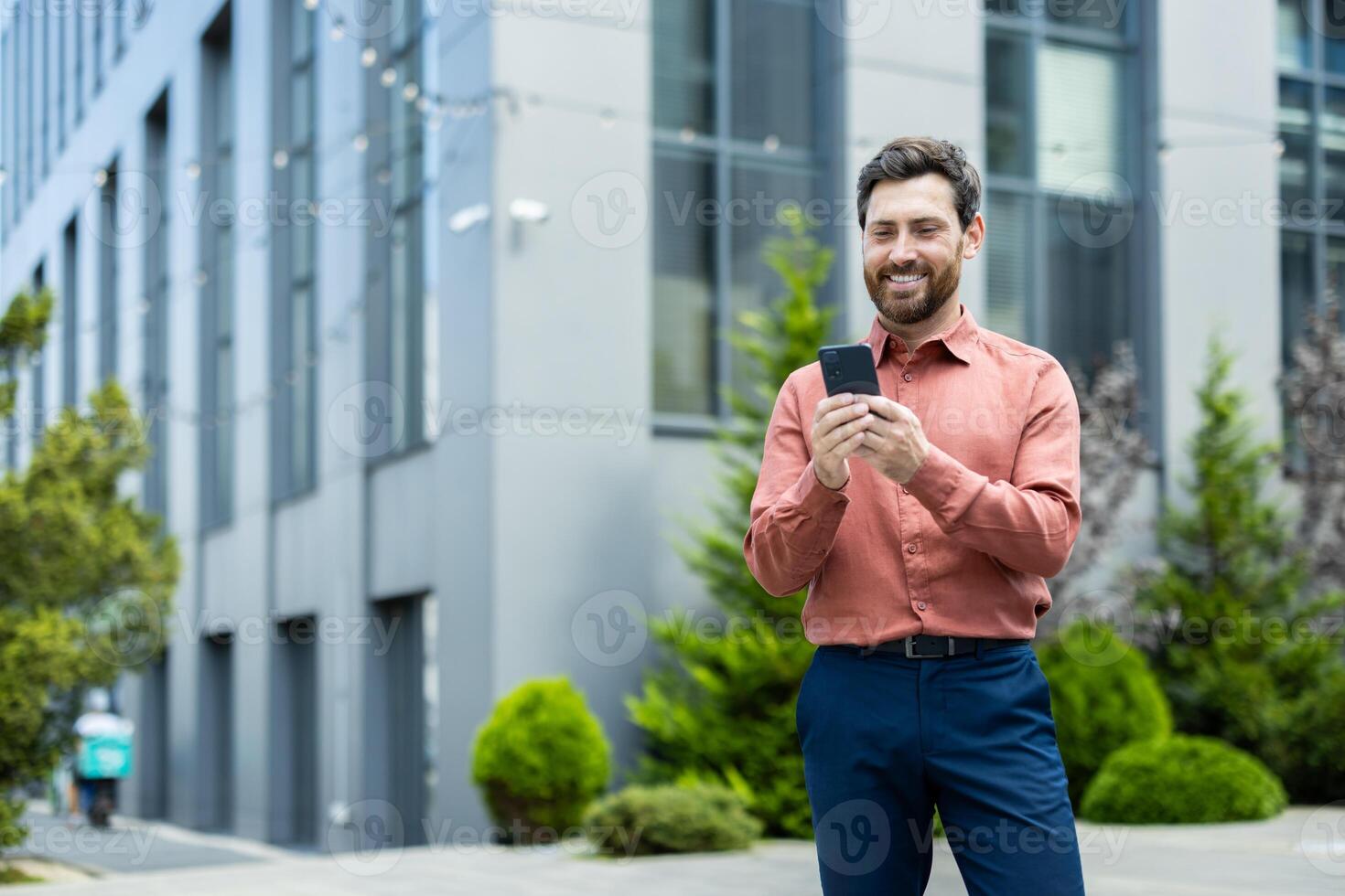 A happy businessman uses his mobile phone outside an office building, smiling as he reads a message or browses the internet. photo