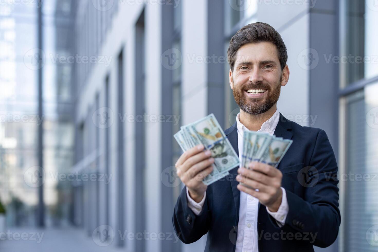 A successful businessman holding cash and smiling confidently in front of an office building, a symbol of wealth. photo