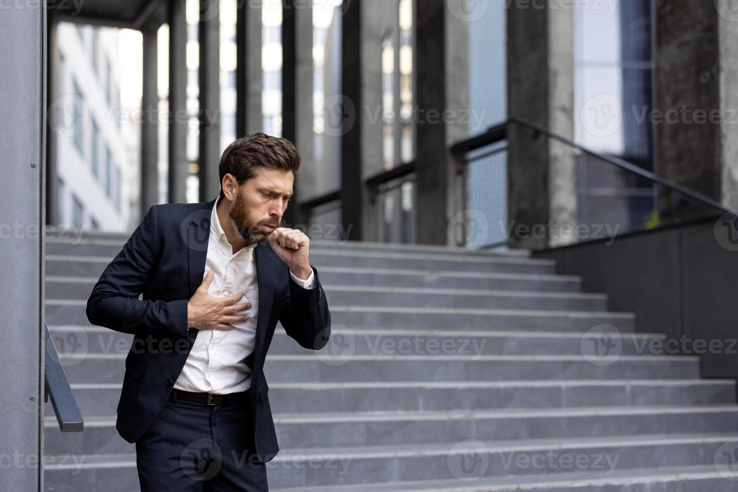 A businessman, clearly unwell, coughs while clutching his chest outdoors. The man is experiencing what seems to be illness or respiratory issues. photo