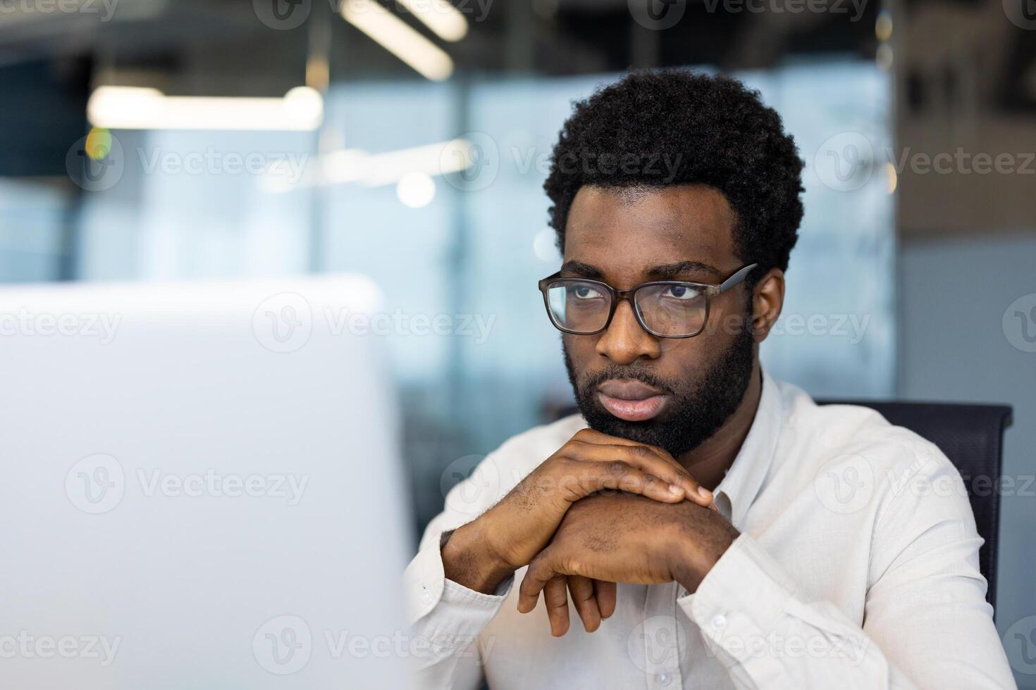 A focused, man wearing glasses looks intently at a computer screen, deep in thought at work. photo