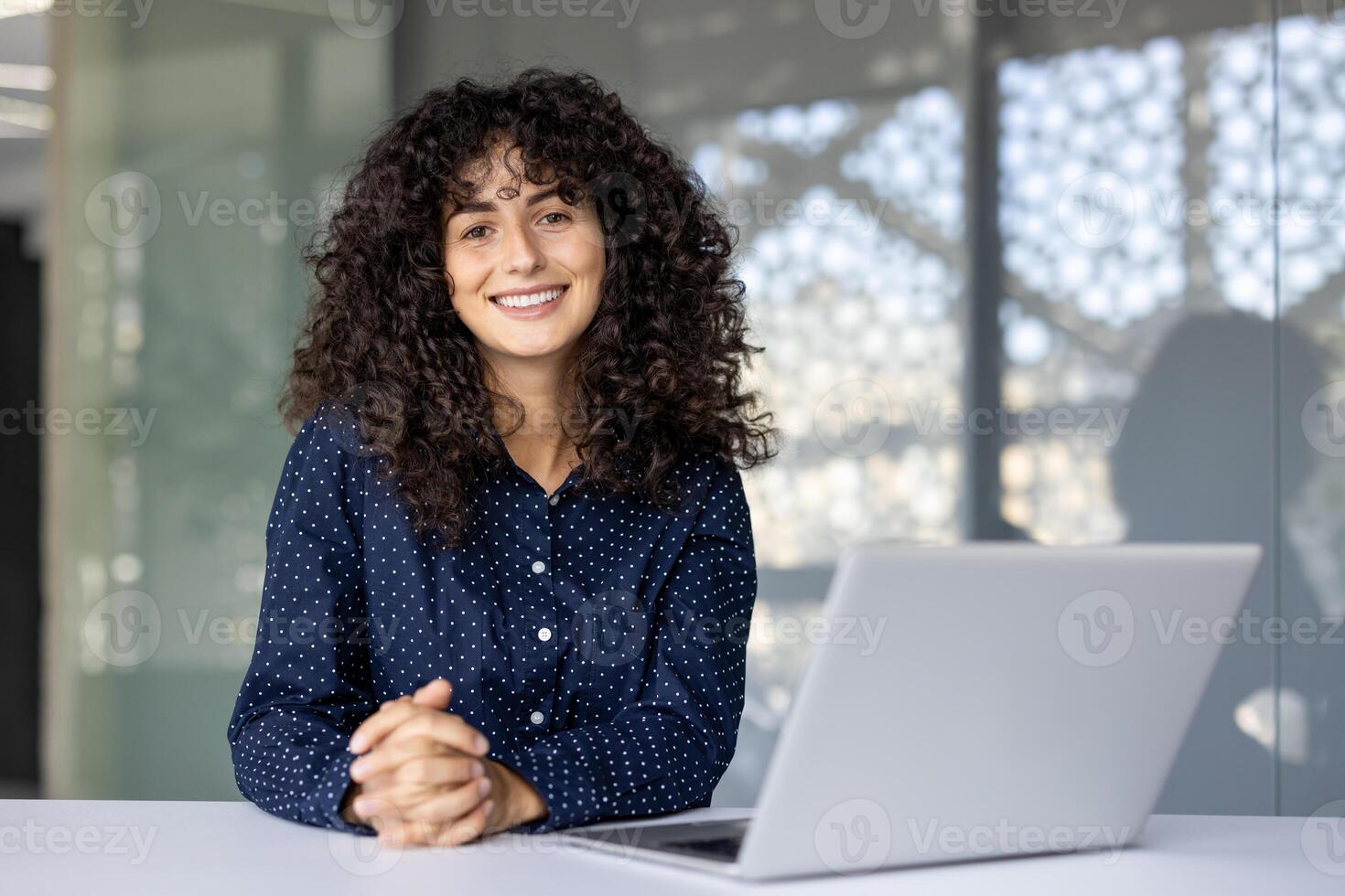 Successful and joyful businesswoman at workplace inside office smiling and looking at camera. Satisfied woman working at desk with laptop. photo
