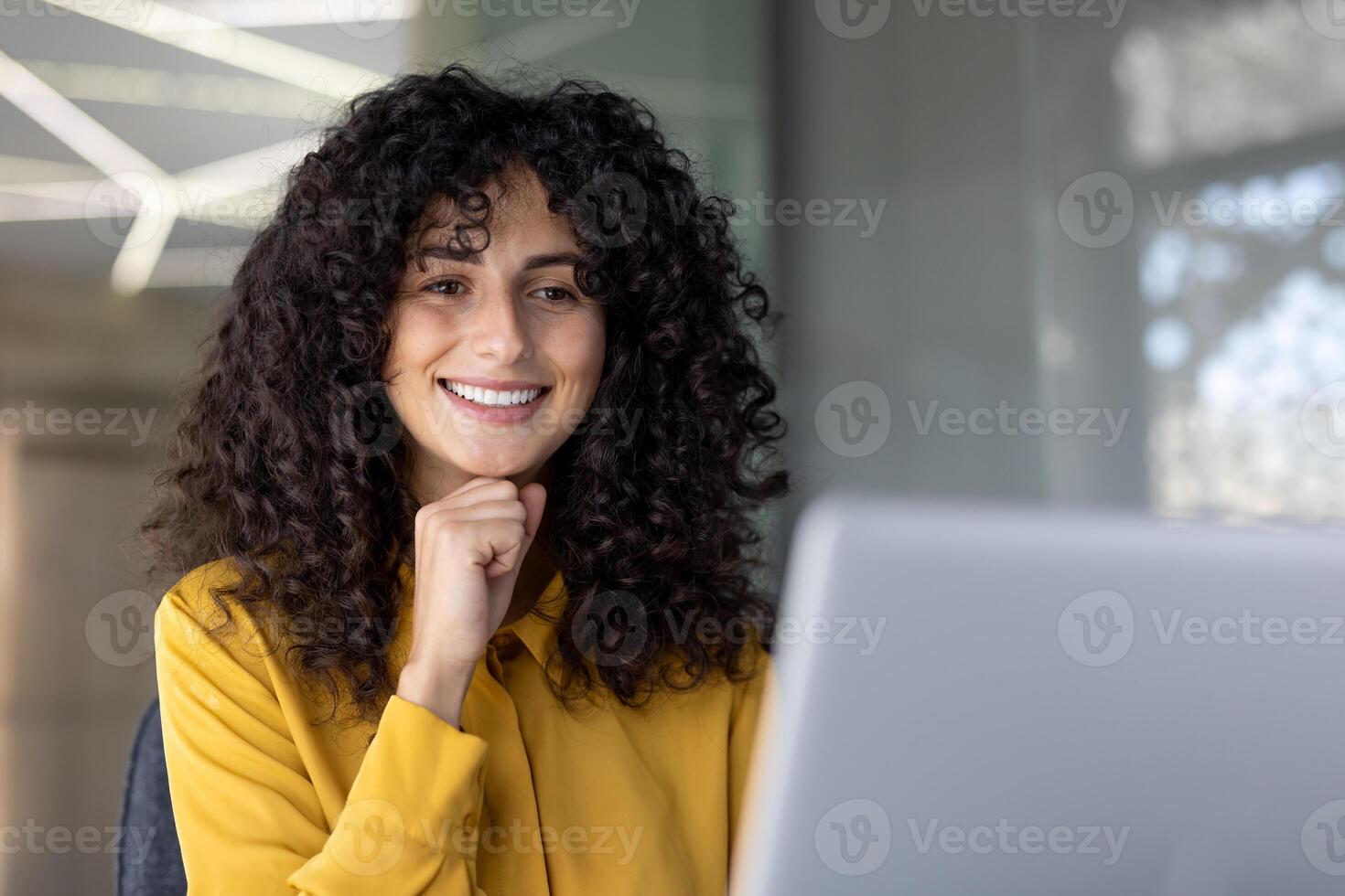 A beautiful woman smiles as she works on a laptop, looking cheerful and content, enjoying a moment of productivity. photo