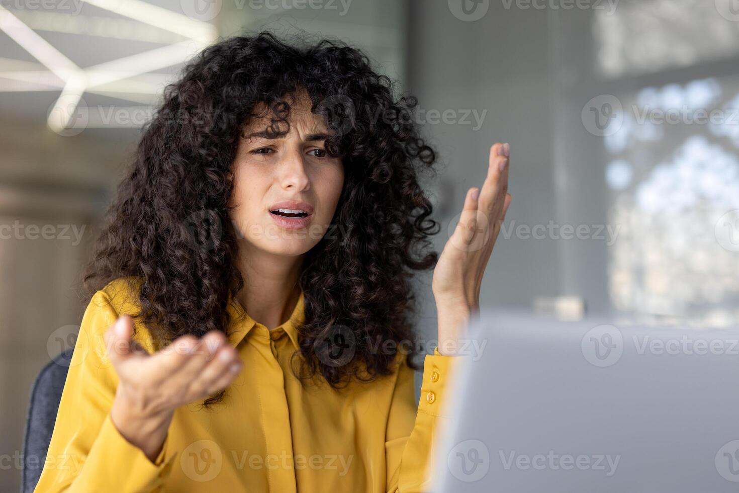 A frustrated woman with curly hair gestures emphatically during a call, looking upset and confused. photo