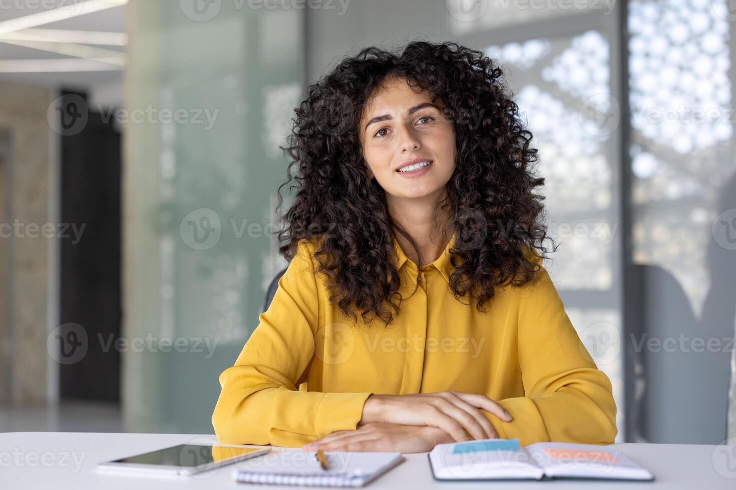 Portrait of a young woman sitting at a desk with a tablet, notebook, and pen, ready to work or study in a bright and modern office space photo