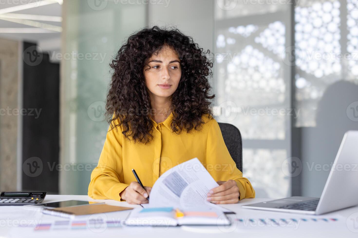 A thoughtful businesswoman reviews documents in her modern office, focused and ready for her work. Natural light illuminates her workspace, creating a bright and professional atmosphere. photo