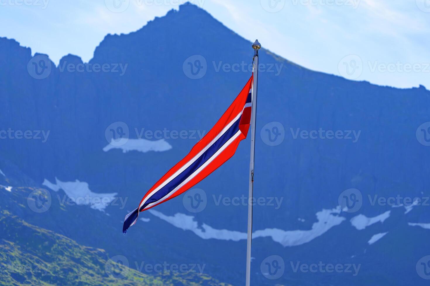 A breathtaking scenic view of the Norwegian flag proudly waving against a backdrop of a majestic mountain range. The vibrant colors and stunning landscape capture the natural beauty of Norway. photo