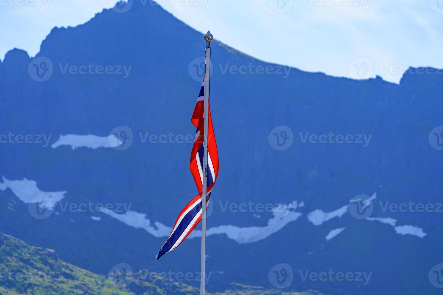 The Norwegian national flag waves proudly in front of a breathtaking mountain range, offering a stunning representation of Norway's natural beauty and national pride. photo