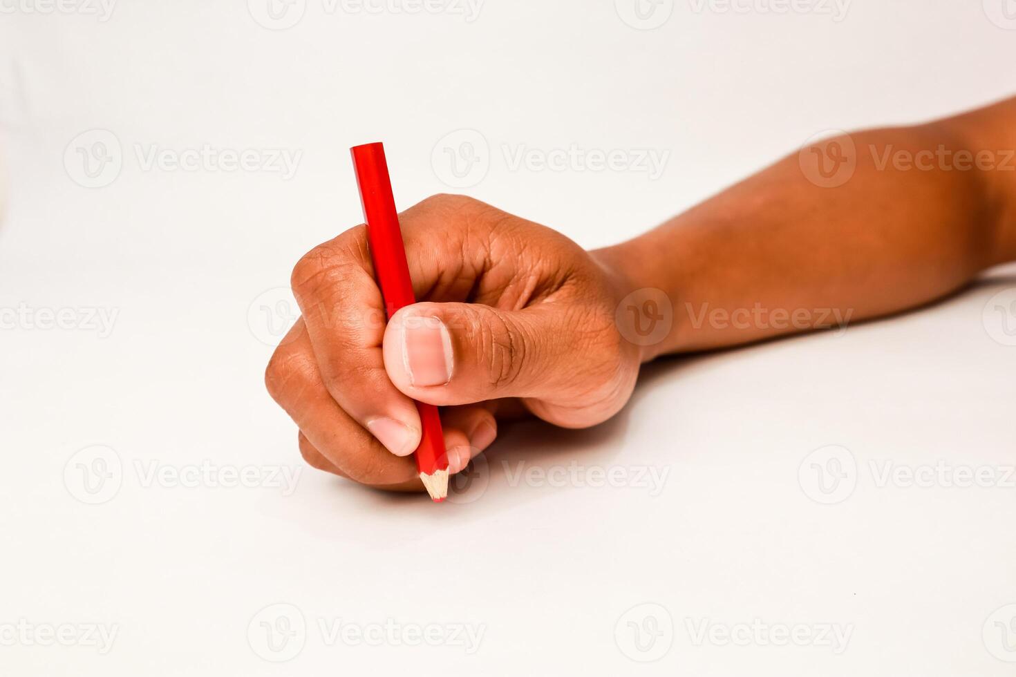 Hand holding a red pencil ready to write on a white surface, creative process photo