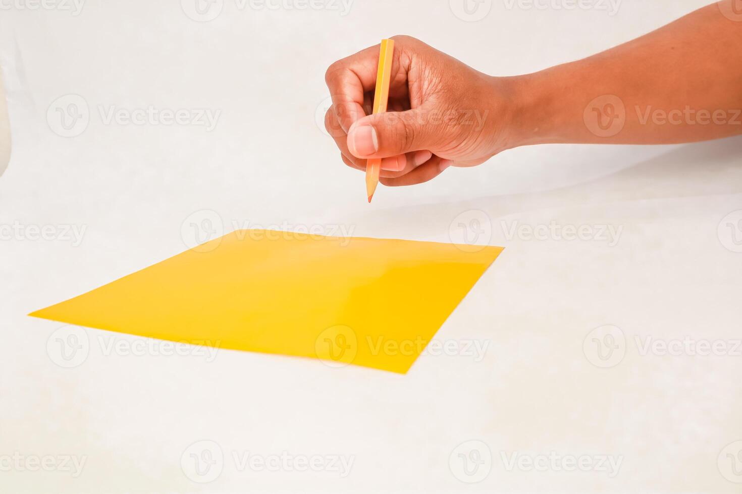 Hand holding a pencil above a yellow sheet of paper ready to draw or write photo