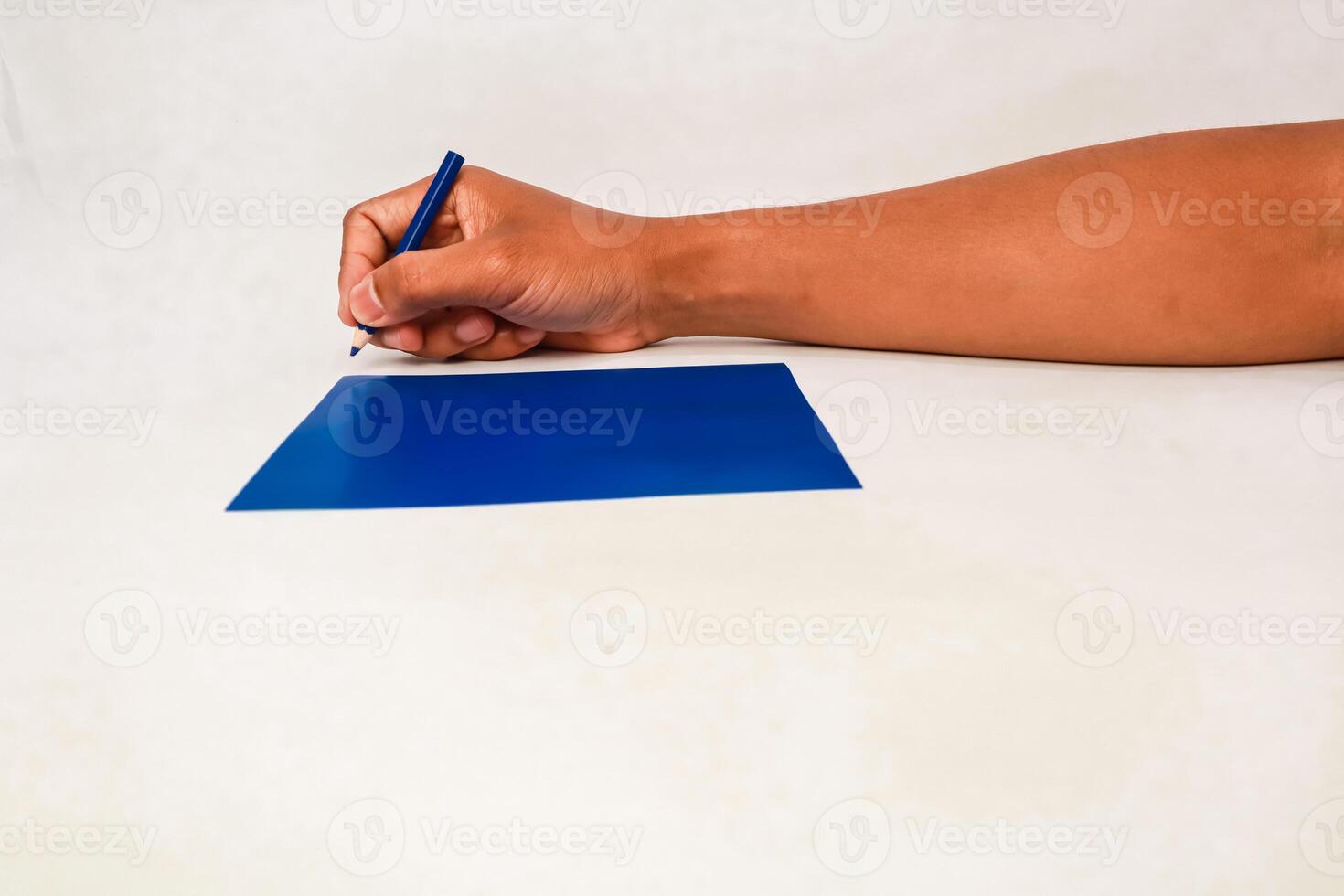 Close-up of a person's hand using a blue pen to write or draw on a blue paper photo