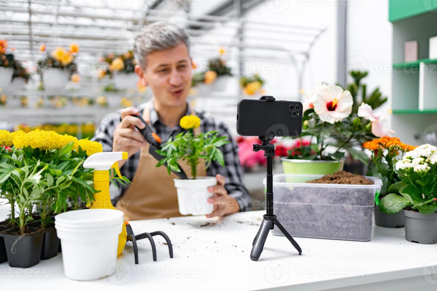 A man records a about gardening with a smartphone. Plants and gardening tools are on a table. photo