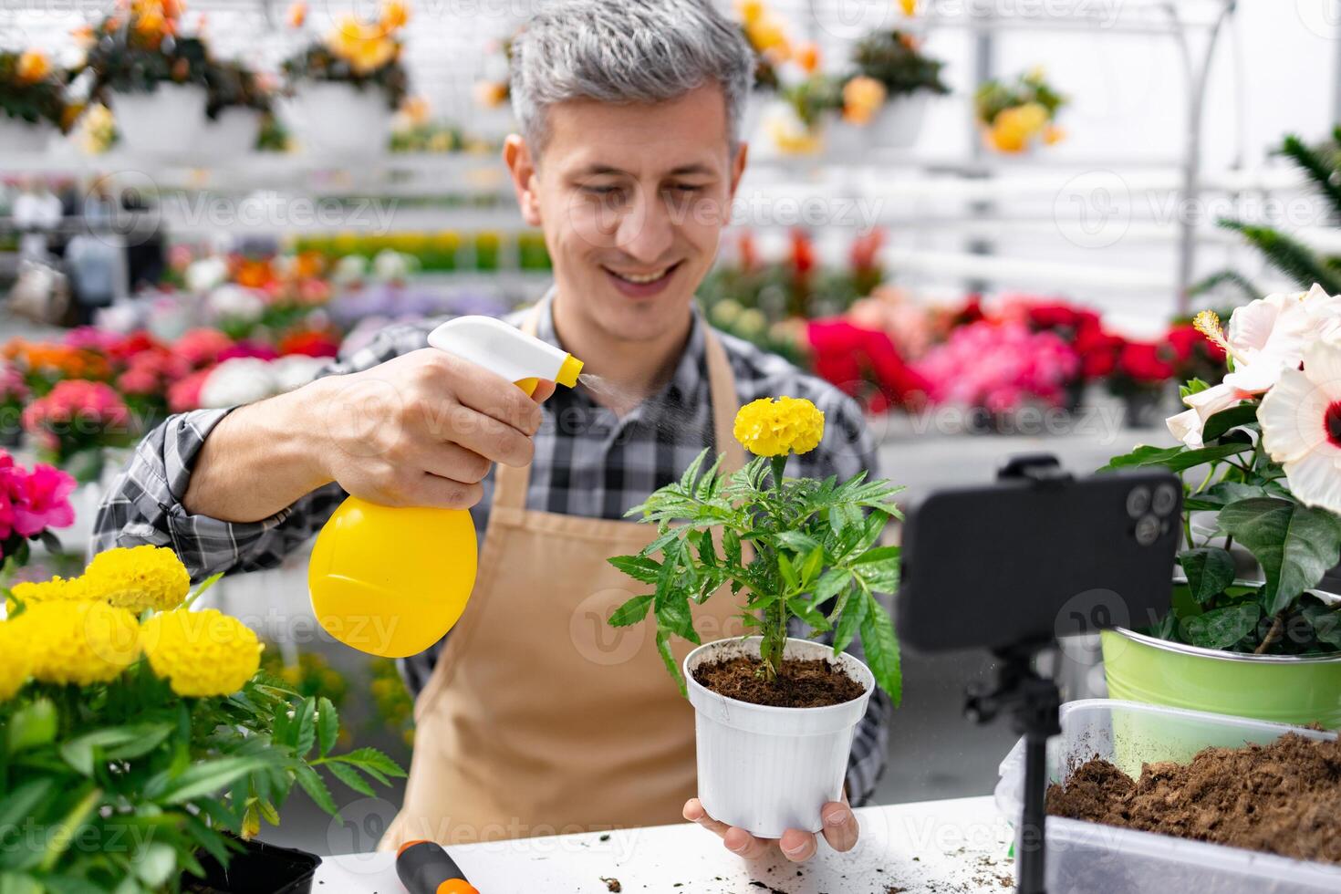 A man in a flower shop waters a plant while filming a tutorial with his phone, teaching online. photo