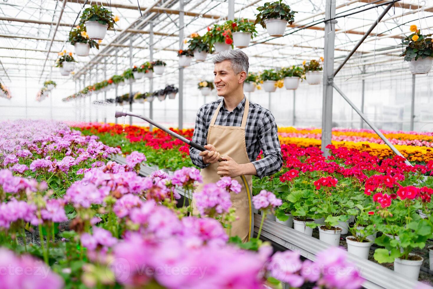 A man waters flowers in a vibrant greenhouse filled with colorful blooms and hanging plants. photo