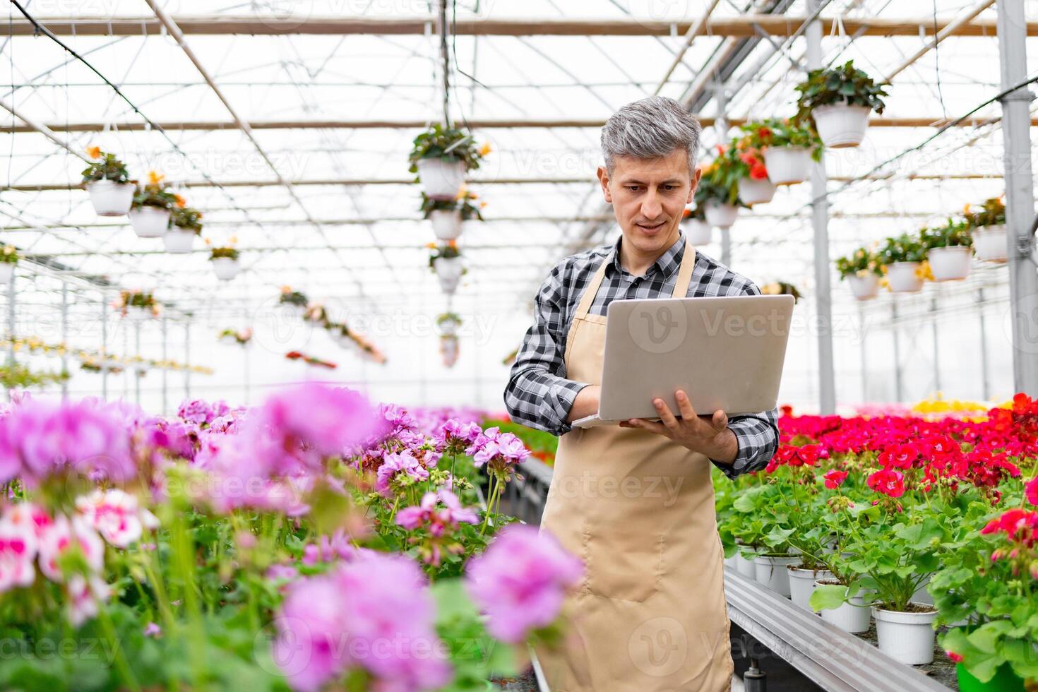 A man in a greenhouse, working on a laptop amidst vibrant flowers, managing plants. photo