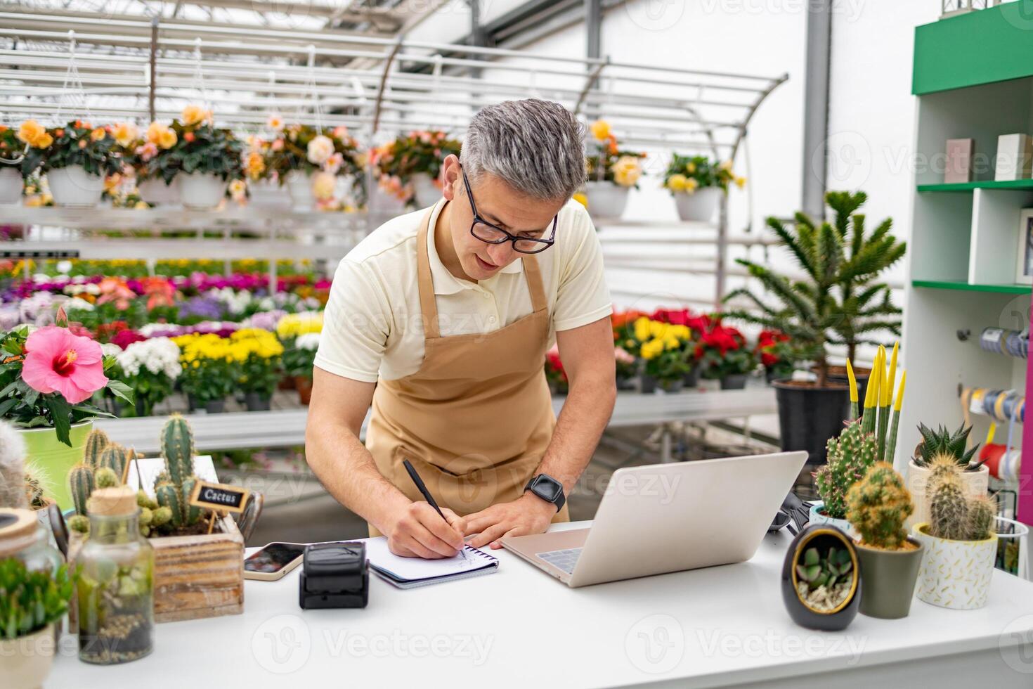 A Caucasian man in a flower shop working on the table, surrounded by plants and flowers. photo