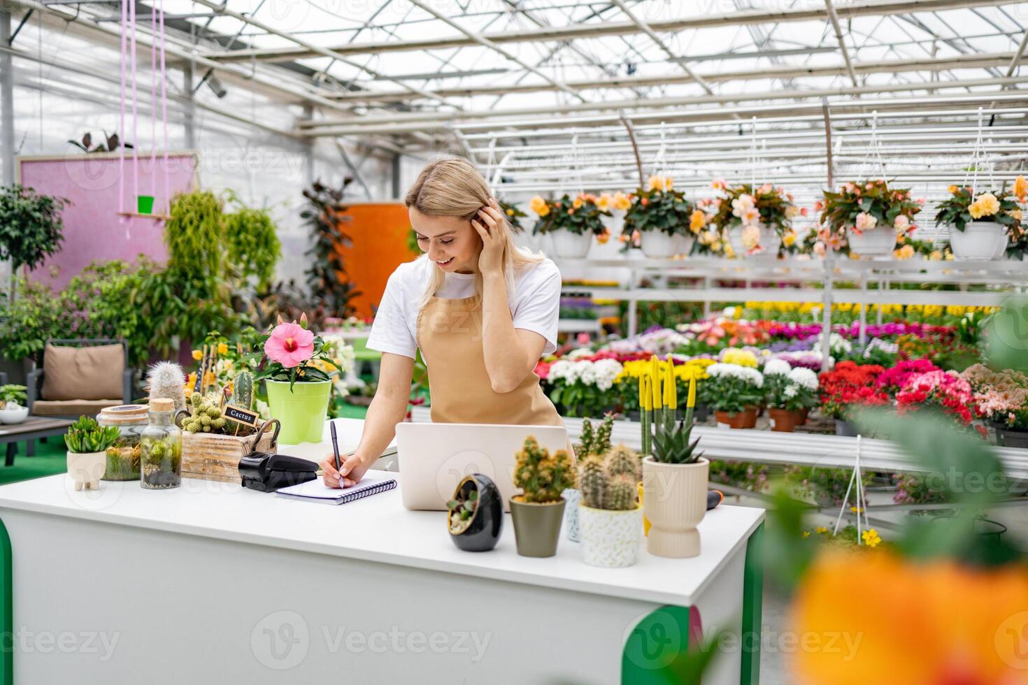 A Caucasian woman in a florist shop, writing in a notebook. She is surrounded by various plants and flowers. photo