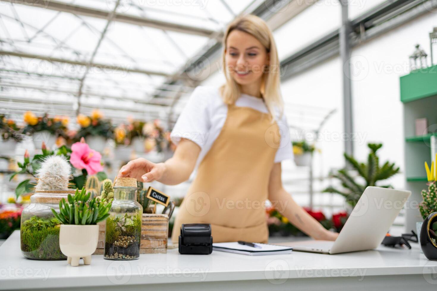 A Caucasian woman in a florist shop is working on a laptop and arranging plants on a table. photo