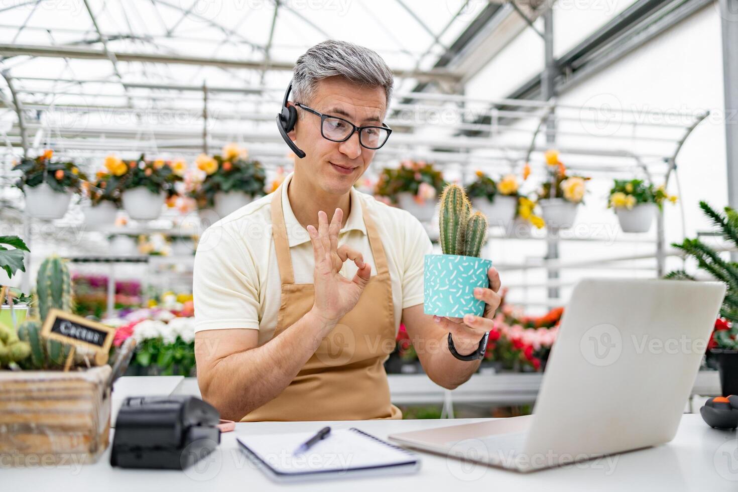 A Caucasian man in a florist shop shows a cactus during a call. He is holding the plant and signaling okay. photo