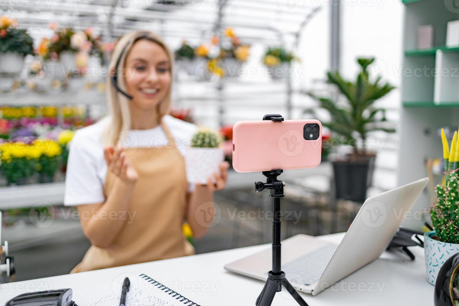 A Caucasian woman in a florist shop hosts a live sale of a cactus, using her smartphone for a broadcast. photo