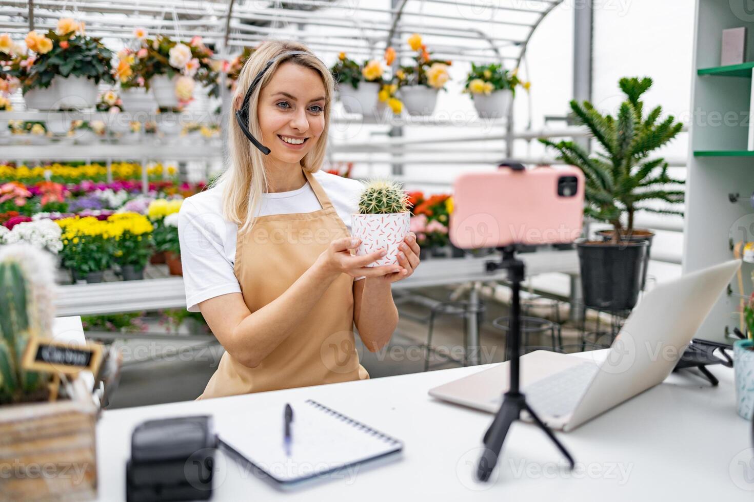 A Caucasian woman in a florist shop is presenting a cactus on camera, live streaming or recording for a sale event. photo