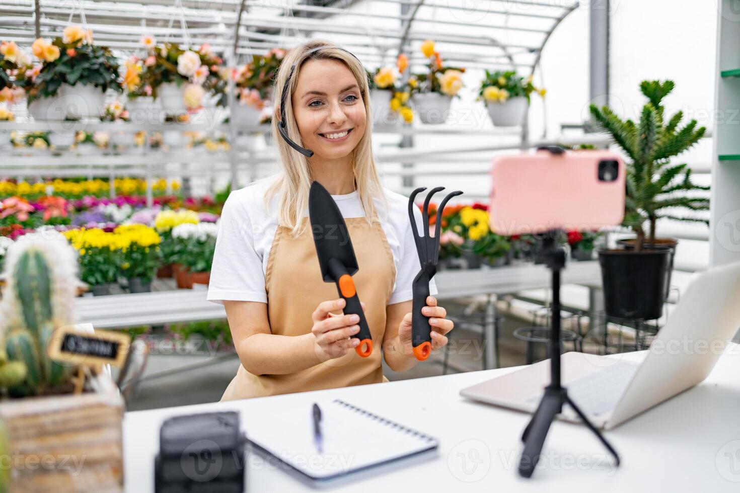 A Caucasian woman, a florist, explains gardening tools in her shop, preparing for a live sale, with a friendly and inviting demeanor. photo