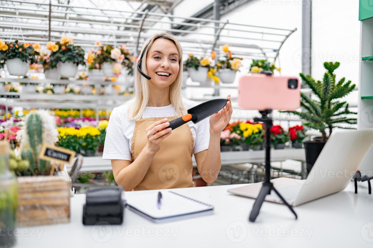 A Caucasian woman florist, demonstrating a garden tool to her audience from inside her shop while doing a live sale. photo