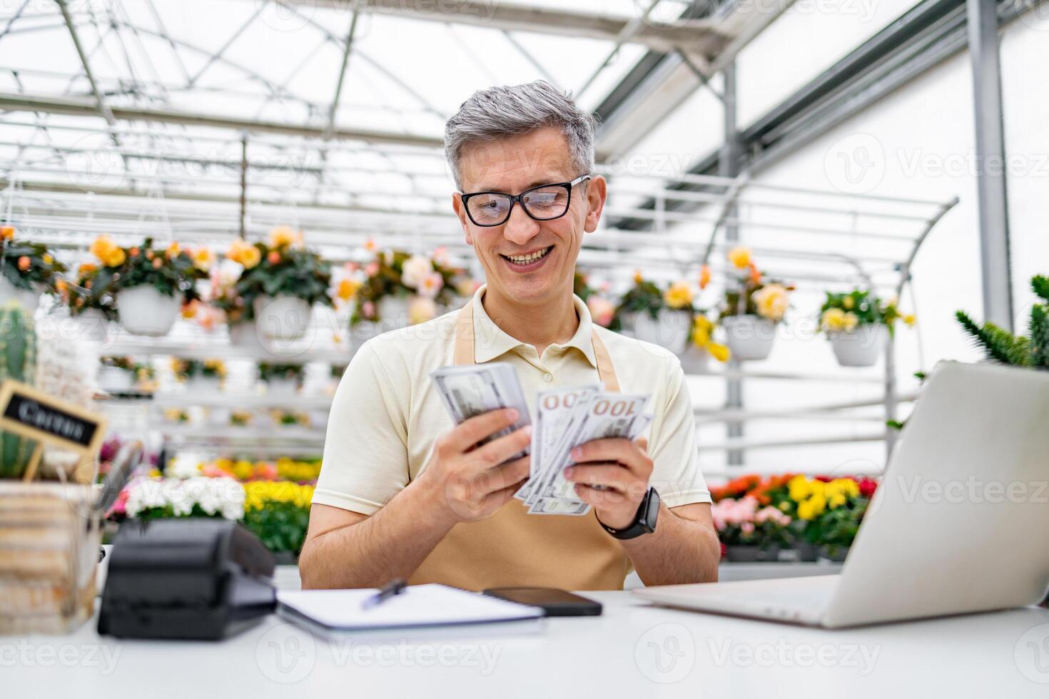 A Caucasian man in a florist shop happily counts his cash sales over the counter. photo