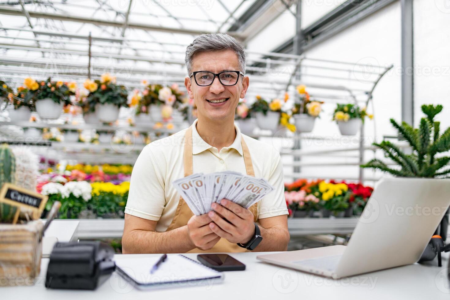 A smiling Caucasian man is holding cash at his shop. The florist stands at the counter in the flower shop. photo