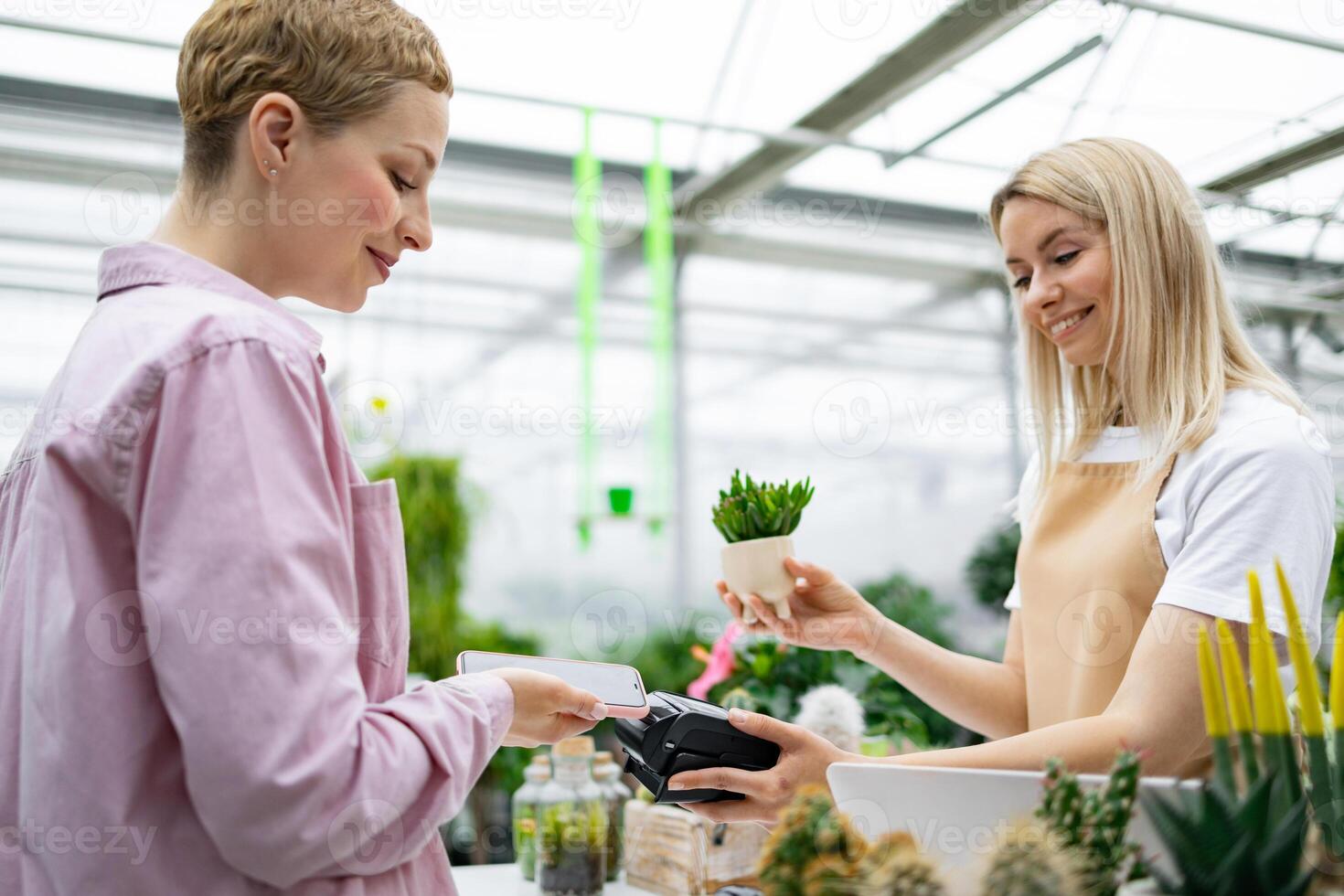 A customer pays for a purchase at a florist shop using a smartphone. The shop assistant is offering a small plant. photo