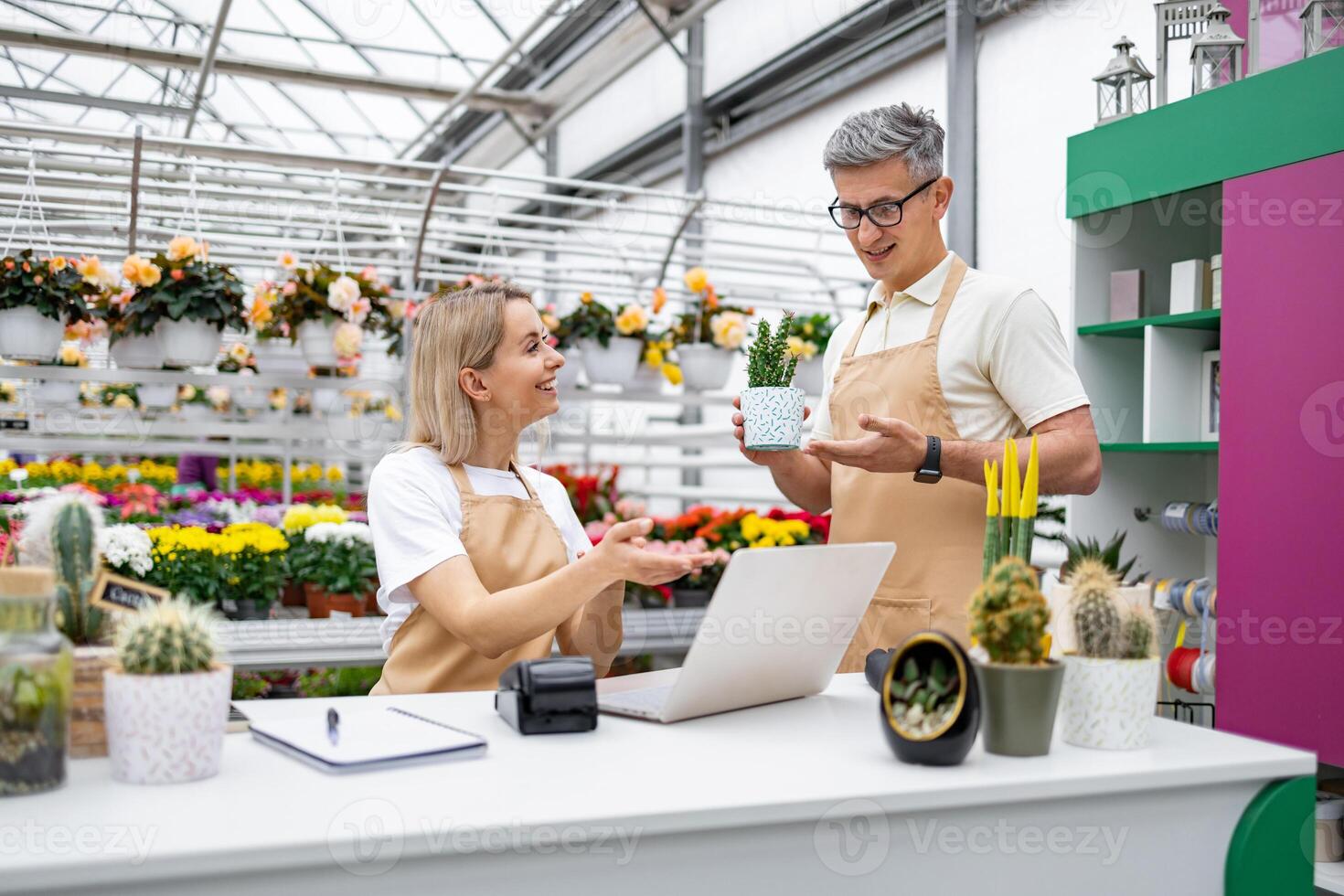 Two florists discuss a plant at the sales counter in a plant shop filled with various flowers and plants for sale. photo
