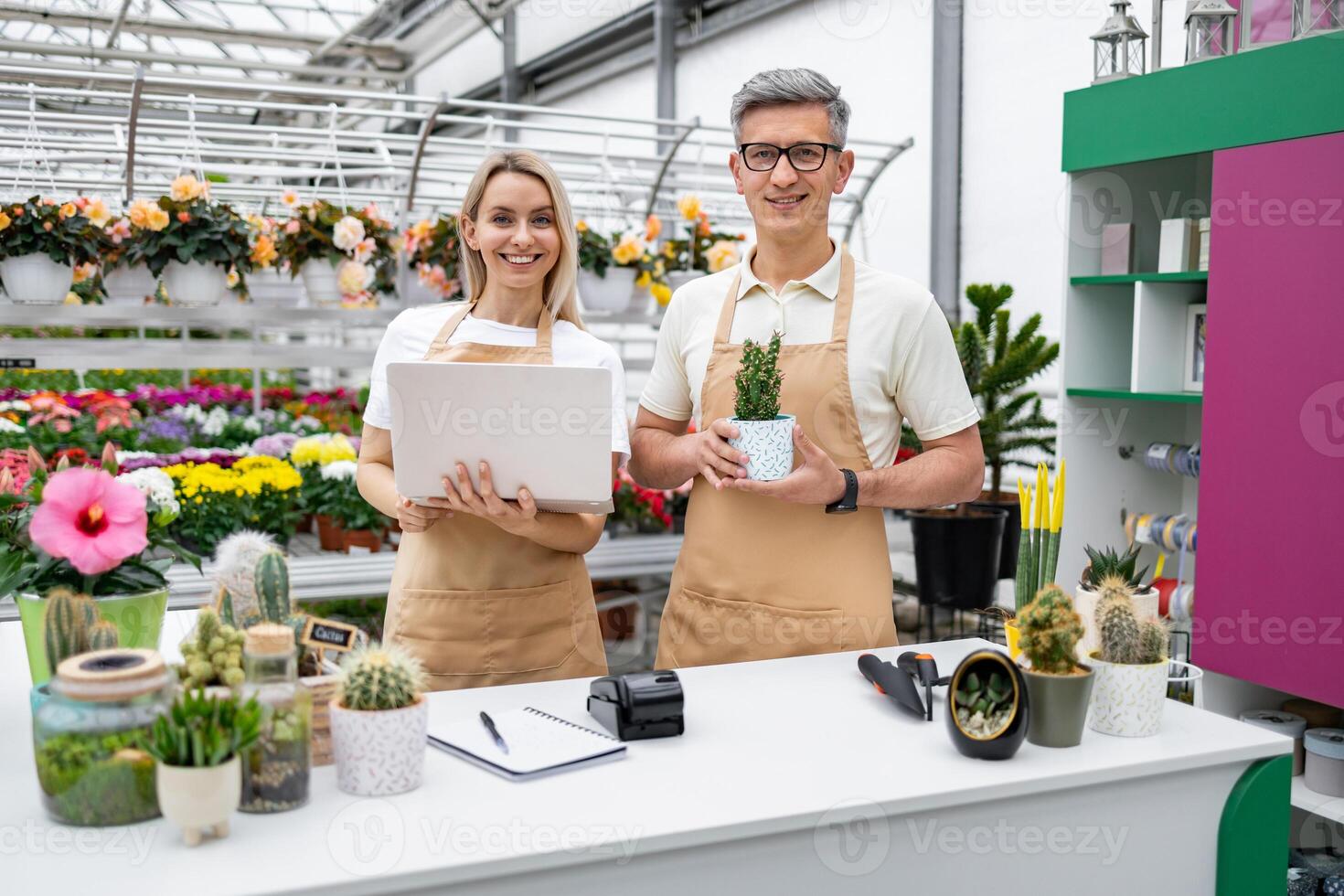 A florist and assistant stand at the counter, ready to serve customers in their plant shop, filled with flowers and plants. photo