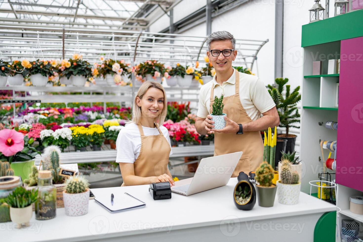 Two florists in a shop setting, presenting the sale of plants and flowers. The Caucasian employees are happy and smiling for the camera. photo
