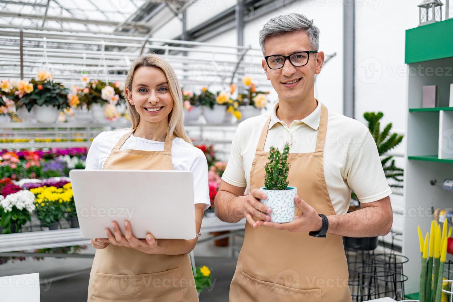 A florist and a colleague smile as they pose with a laptop and a small potted plant in their shop. photo