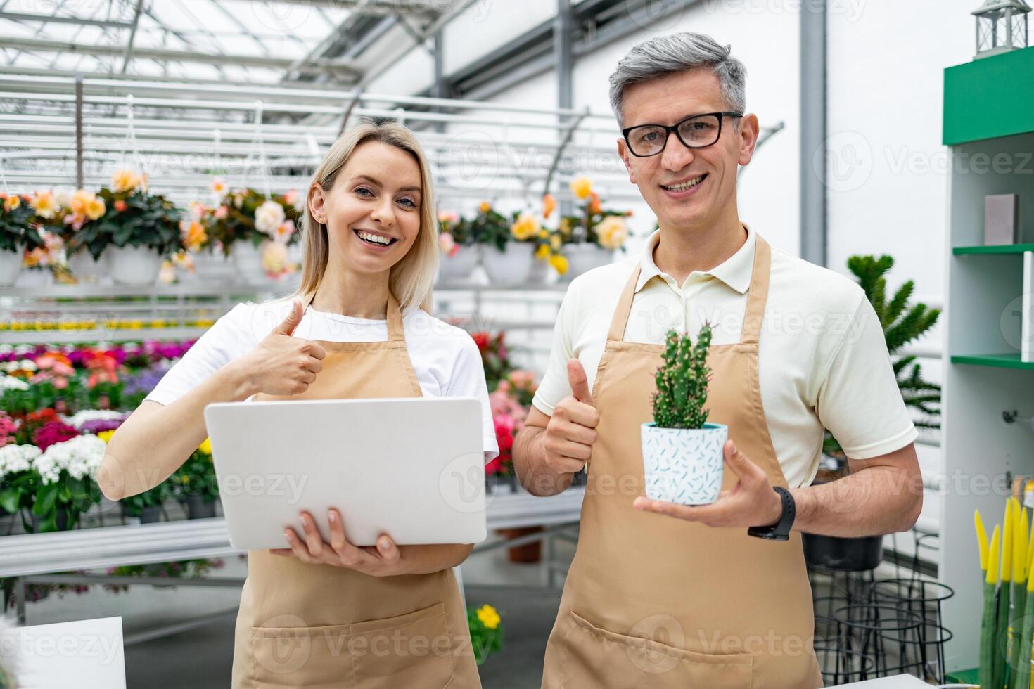 Happy florists with a laptop and potted plant give a thumbs up, showing their approval in the shop, with plenty of flowers. photo