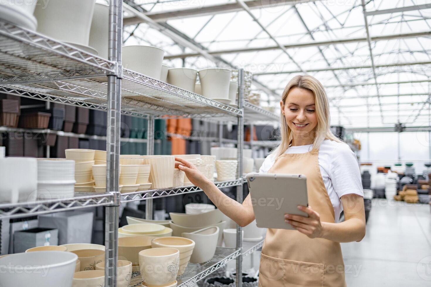A shop assistant with a tablet inspects shelves stocked with various flowerpots, preparing for inventory. photo