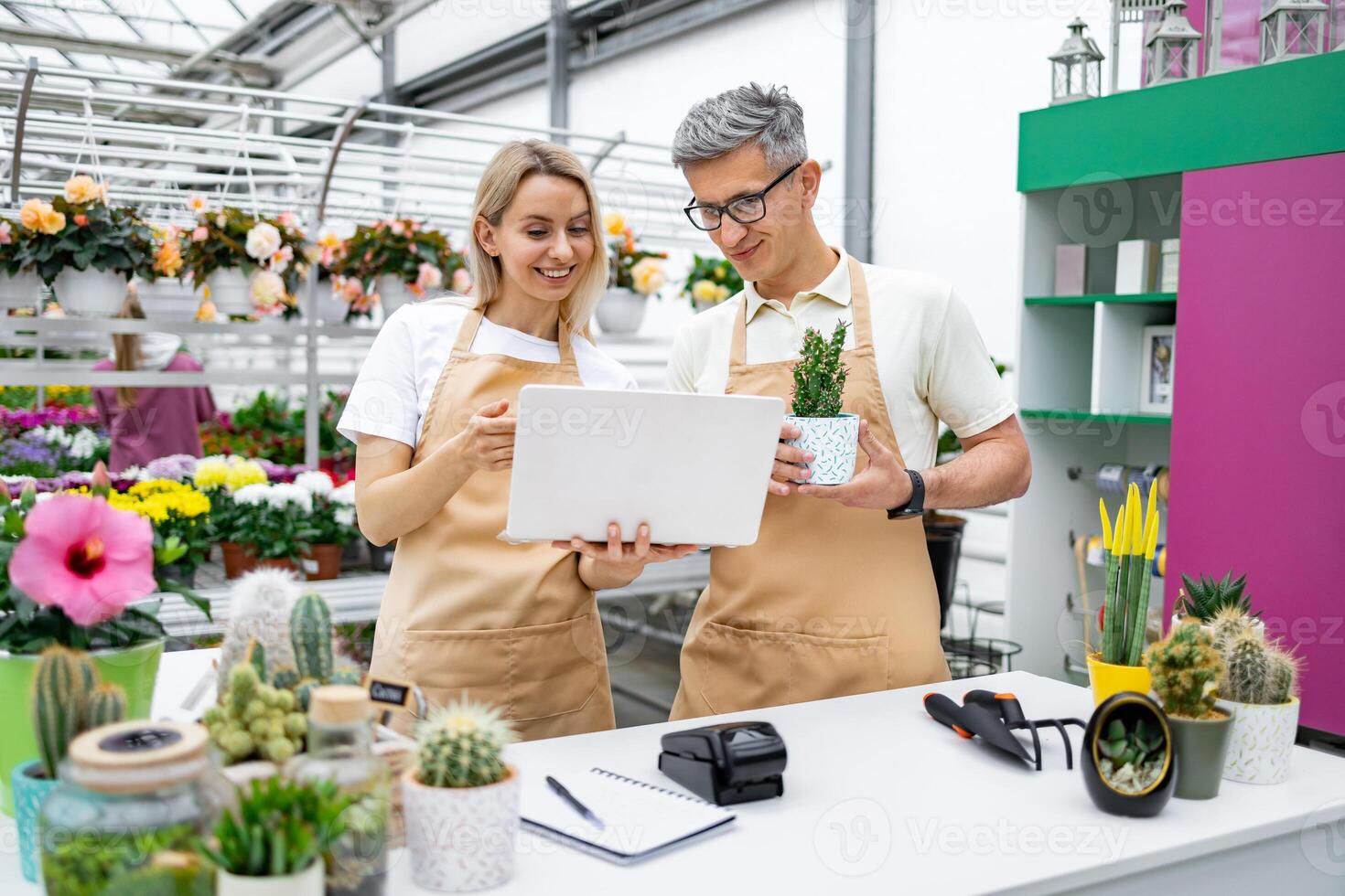A florist and a customer checking a laptop while at a sale table in the shop. The woman is holding the laptop, and the man is holding a potted plant. photo