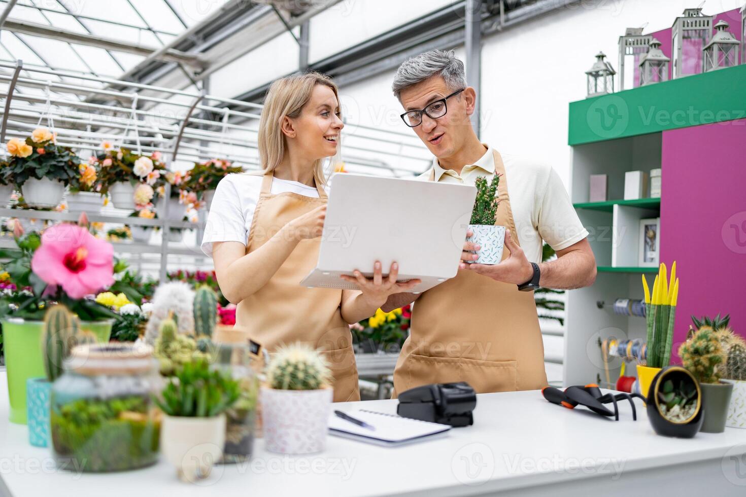 A florist and a shop owner, both Caucasian, look at a laptop. The image captures a scene of a sale table. photo