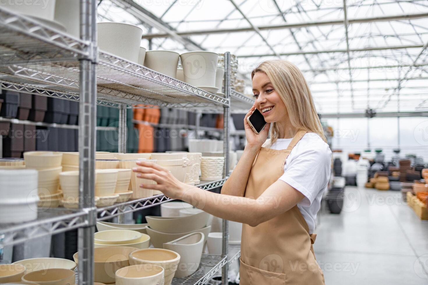 A woman is on the phone at a shop, looking at a variety of flowerpots. photo