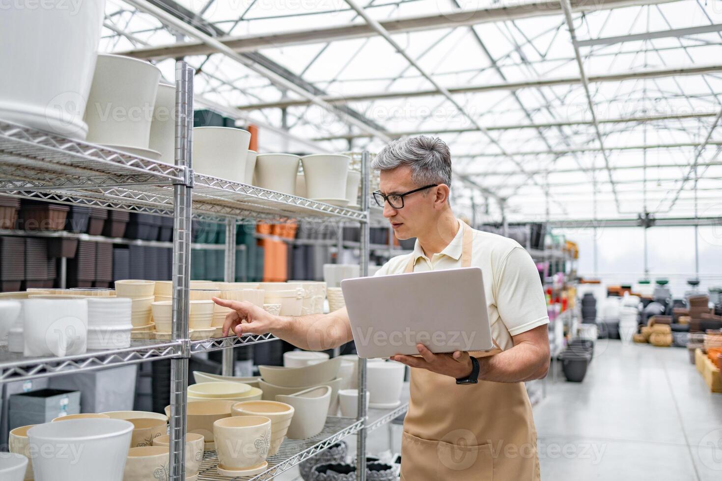 A man in a shop with a laptop looks at the flowerpots on the shelves, browsing and making a choice. photo