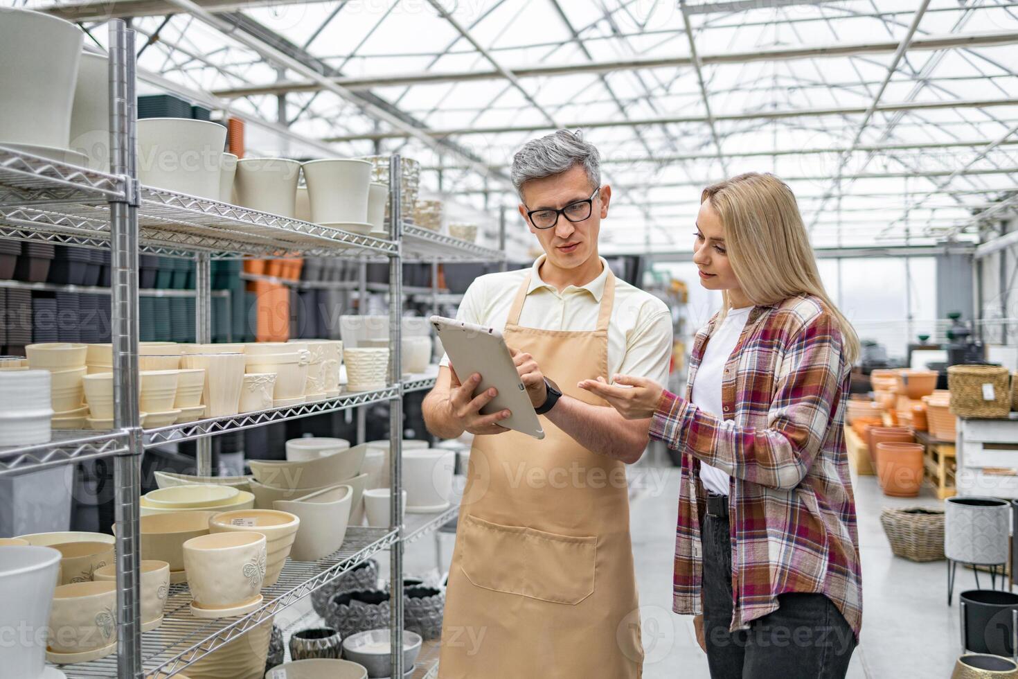 A flower shop employee assisting a customer in choosing the perfect flowerpots using a digital tablet, with shelves of various ceramic pots. photo